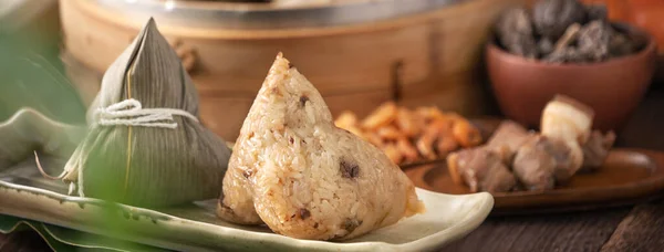 Rice dumpling - Chinese zongzi food in a steamer on wooden table with red brick wall, window background at home for Dragon Boat Festival concept, close up.