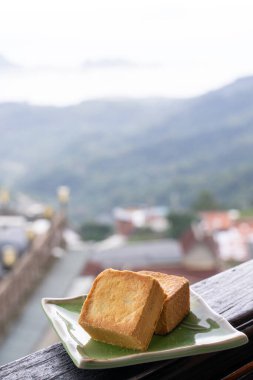 Delicious pineapple pastry in a plate for afternoon tea on wooden railing of a teahouse in Taiwan with beautiful landscape in background, close up.