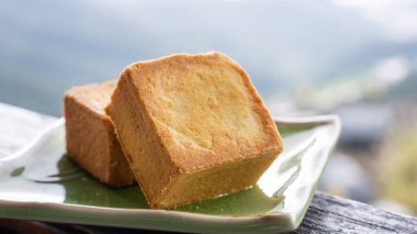 Delicious pineapple pastry in a plate for afternoon tea on wooden railing of a teahouse in Taiwan with beautiful landscape in background, close up.