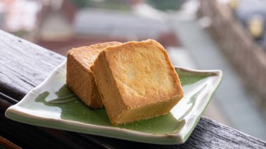Delicious pineapple pastry in a plate for afternoon tea on wooden railing of a teahouse in Taiwan with beautiful landscape in background, close up.