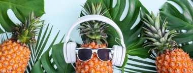 Beyaz kulaklık takan komik ananas, müzik dinleme konsepti, tropik palmiye yaprakları ile izole edilmiş renkli arka plan, üst görünüm, düz dizayn.