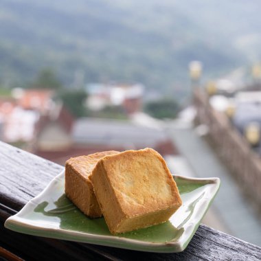 Delicious pineapple pastry in a plate for afternoon tea on wooden railing of a teahouse in Taiwan with beautiful landscape in background, close up.
