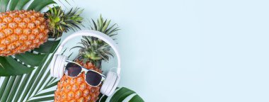 Beyaz kulaklık takan komik ananas, müzik dinleme konsepti, tropik palmiye yaprakları ile izole edilmiş renkli arka plan, üst görünüm, düz dizayn.