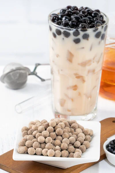 Bubble milk tea with tapioca pearl topping ingredient, famous Taiwanese drink on white wooden table background in drinking glass, close up, copy space