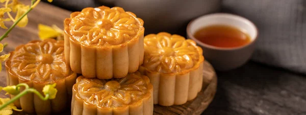 Mooncake, Moon cake for Mid-Autumn Festival, concept of traditional festive food on black slate table with tea and yellow flower, close up, copy space.