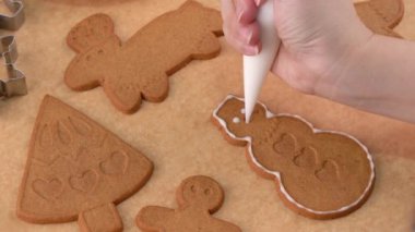 Genç bir kadın evde Noel kurabiyesi bisküvisi süslüyor. Krema torbasıyla süslenmiş, yakın plan, yaşam tarzı..