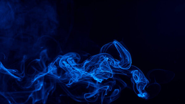 Conceptual image of blue color smoke isolated on dark black background, Halloween design element concept.