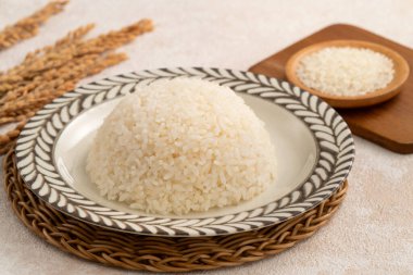 Bir kase taze pişmiş beyaz pirinç, yumuşak, kabarık ve beyaz masa arkasında hafifçe parıltılı..