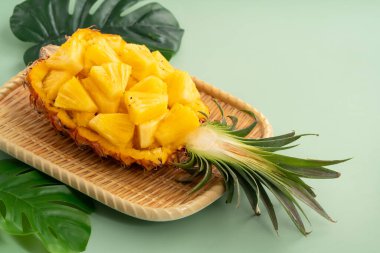 Arkaplanda tropik yapraklar olan yarım bir ananas kasesine yerleştirilmiş sulu ananas parçaları..