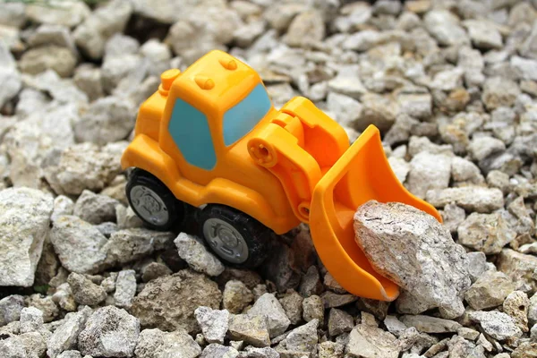 Mały pomarańczowy Digger zabawka podnosi szare kamienie — Zdjęcie stockowe