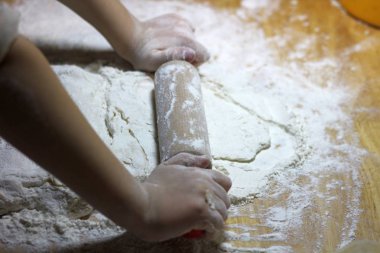 Çocukların elleri ve hamuru. Küçük çocuk hamur yoğuruyor. Sağlıklı el yapımı gıda konsepti. fırın ürünleri, pizza, un. yemek atölyesi. bebeğin elleri ahşap bir masaüzerinde bir hamur dışarı rulo.