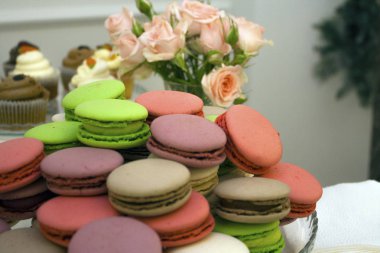 arka plan olarak gül ile bir tabakta renkli macarons kek