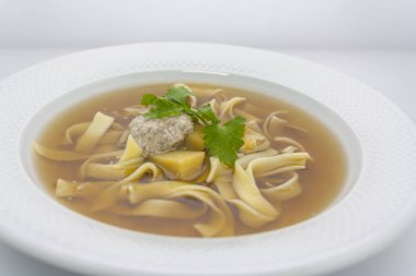 Bir restoranda beyaz bir tabakta maydanoz ile patates ve buğday sosu ile Geleneksel Avrupa şeffaf sığır şehriye çorbası