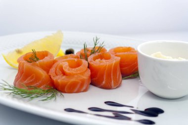 beyaz bir tabakta limon, kapari, ekşi krema sosu ve dereotu ile somon rulo