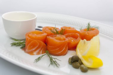 limon ile somon rulo, kapari, ekşi krema sosu ve dereotu beyaz bir tabak üzerinde yakın