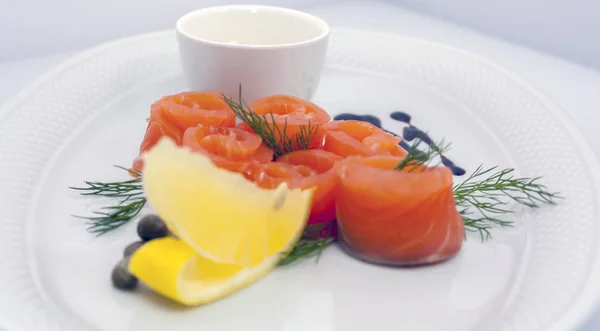 salmon rolls with lemon, capers, sour cream sauce and dill on a white plate