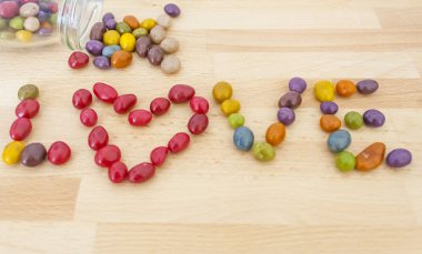 ahşap bir tahta üzerinde çok renkli şekerler dışarı serilir kelime aşk