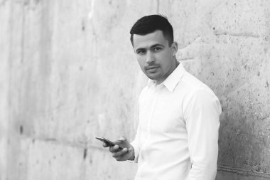 sokakta duvara yakın akıllı telefon ile ayakta beyaz gömlek yakışıklı işadamı