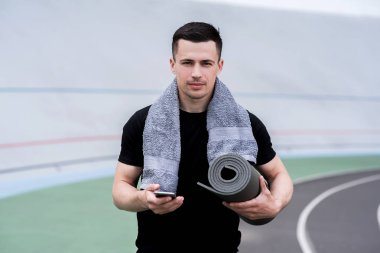 stadyumda akıllı telefon kullanarak havlu ile yakışıklı sporcu 