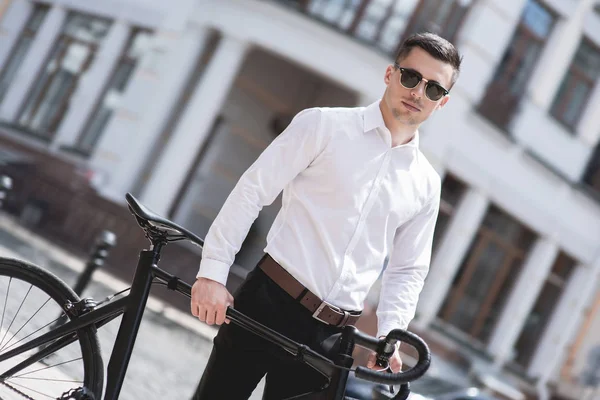 handsome man in shirt walking with bicycle in city