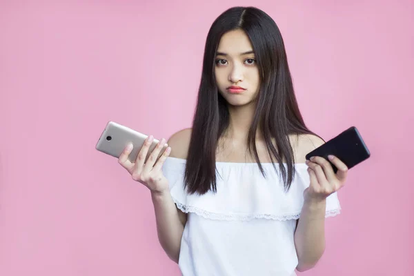 sad asian girl holding smartphones on pink background