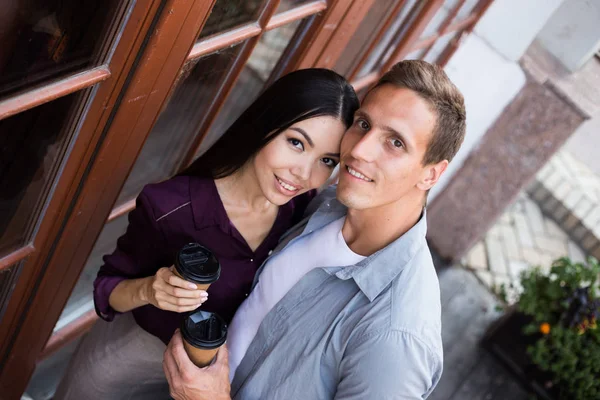 Vrolijke Jonge Paar Met Wegwerp Koffie Kopjes Kijken Naar Camera — Stockfoto