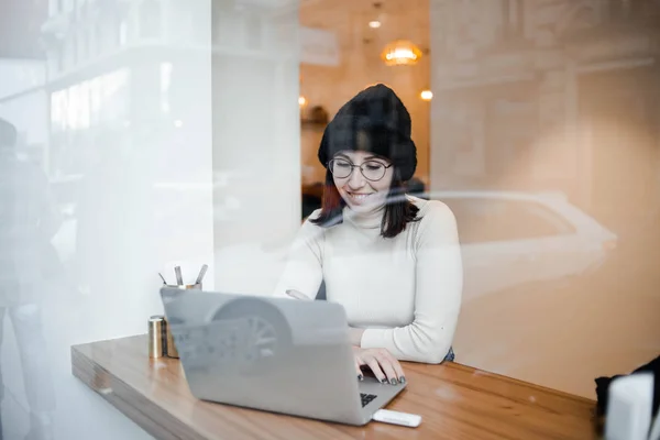 迷人的年轻自由职业者戴着眼镜坐在街头咖啡馆与她的上网本 看着屏幕 — 图库照片