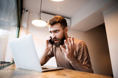 Kızgın patron çalışma sürecinde ki hatalar hakkında iş arkadaşıyla konuşurken cep telefonundan bağırıyor.adam işadamı başarısız başlangıç projesi hatası nedeniyle işten işçi fuarlığı konusunda yüksek sesle bağırıyor