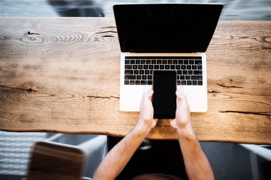 Kablosuz bağlanırken büyük cep telefonu tutan erkek ellerini kapatın, modern çatı ahşap masada oturan teknolojiyi kullanan işadamı, insanlar ve modern cihazlar. Programcı, It işçi, 5g
