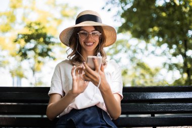 Online eğitim ve bazı öğreticiler listerning, internet ve modern iletişim online arama. Parkta oturan ve kulaklıkbir şey listerning Pretty kadın