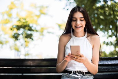 Genç kadın beyaz kulaklıklarla on line müzik uygulaması ile sokakta müzik dinliyor. Pretty gülümseme ve online kavram.