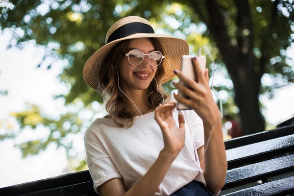 Modern education program on smartphone. Cute woman walking in summer day in hat and smile. She holding phone