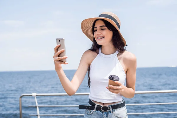 女人站在湖边 在阳光明媚的夏日里使用智能手机 她微笑着 享受着假期的快乐时刻 — 图库照片