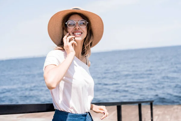 海で晴れた日に美しい港町の背景に携帯電話で話している帽子の若い美しい女性旅行者 冒険と航海 — ストック写真