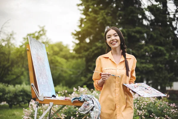 Genç bir kadın sanatçı bir fırça tutar ve gün batımı ışınları bir şöne bir resim boyar. Ressam gün batımında yağlıboya tablolar çiziyor. Blogger sanatçı ressam ev bahçesinde video dersleri yapıyor