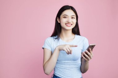 pembe arka planda akıllı telefon kullanarak çekici gülümseyen asyalı kız