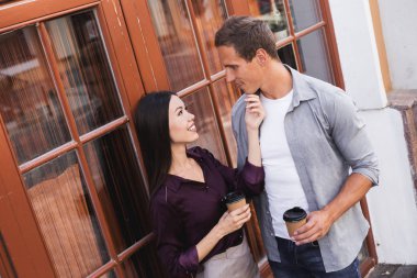 tek kullanımlık kahve fincanları tutan ve kafenin girişinde duran neşeli genç çift