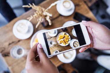 Hipster akıllı telefon tutan, kahve dükkanında lezzetli gıda ve doğal organik kahve mobil fotoğraf çekmek. Blogger blog yazısı için gıda fotoğrafçılığı yapma.