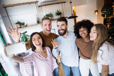 Bir grup arkadaş öğle yemeği yiyor ve birlikte evde modern iç mekanda akıllı telefonla selfie çekiyor 