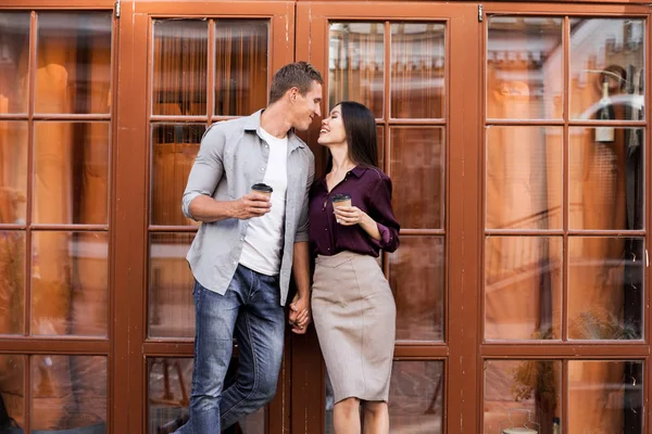 tek kullanımlık kahve fincanları tutan neşeli genç çift ve kafegirişinde yakın öpmek için gidiyor