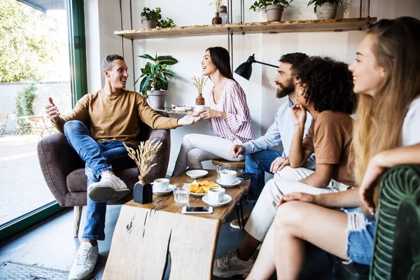 Modern bir kafenin iç mekanlarında oturan, birlikte eğlenen, kahve içen ve eğlenen bir grup genç