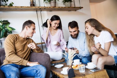 Modern bir kafenin iç mekanlarında oturan, birlikte eğlenen, kahve içen ve eğlenen bir grup genç