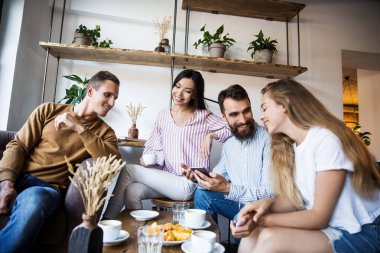 Modern bir kafenin iç mekanlarında oturan, birlikte eğlenen, kahve içen ve eğlenen bir grup genç