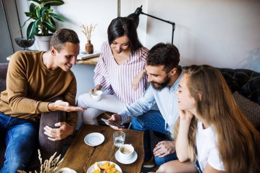 Modern bir kafenin iç mekanlarında oturan, birlikte eğlenen, kahve içen ve eğlenen bir grup genç