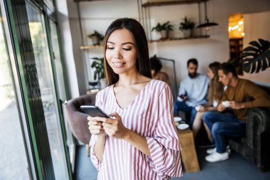 Güzel genç kadın iş adamları bir sürü bulanık arka plan önünde bir metin mesajı göndermek için akıllı telefon cihazında bir uygulama kullanıyor