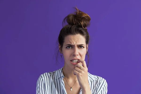 skeptical woman biting nails and looking at camera on violet background