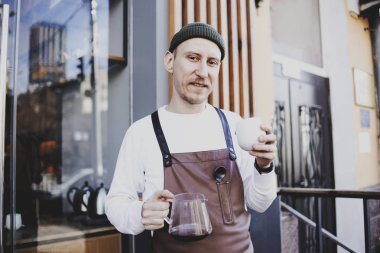 Profesyonel barista kendi iş sahibi, onun kahve dükkanı yakınında sokakta duran ve filtre damla kahve tutarak. Başarı hipster adam, mutlu kendine güvenen insanlar kavramı. Şık ve modaya uygun bir adam 