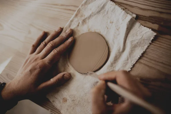 一个女陶工的特写顶部视图是用砖头状的粘土做的 在车间的木制桌子上有一个大的平板 陶瓷车间带滚针的女性陶工模塑粘土 — 图库照片
