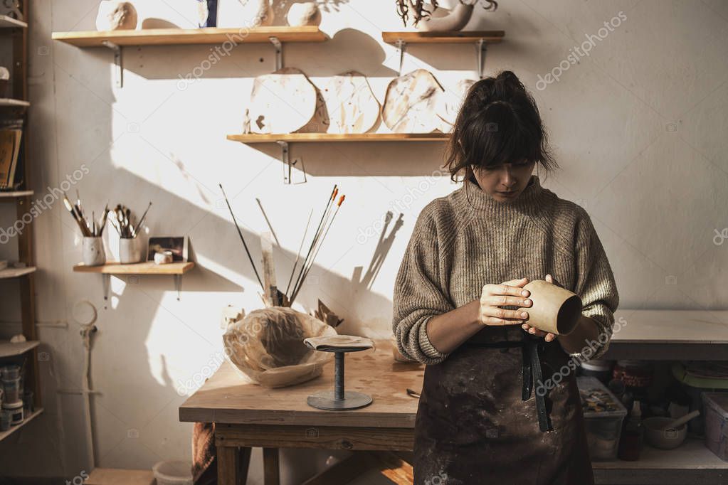 Professional female woman potter on her creative art studio in process creating and modeling new handmade sculpture clay dishes or something for interior. Creative profession, manufacture. Art space