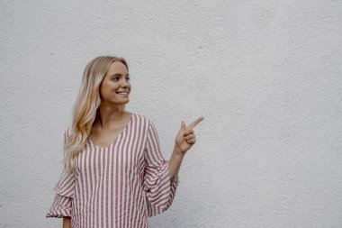 sokakta gri duvara yakın bir şey işaret gülümseyen çekici sarışın kadın